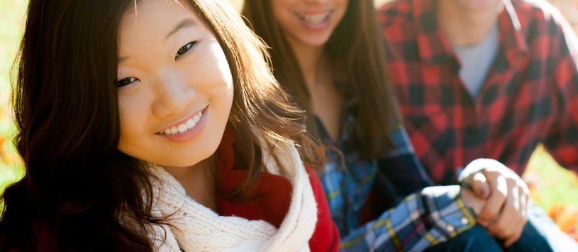 A Korean woman sitting on a field and smiling with other international students