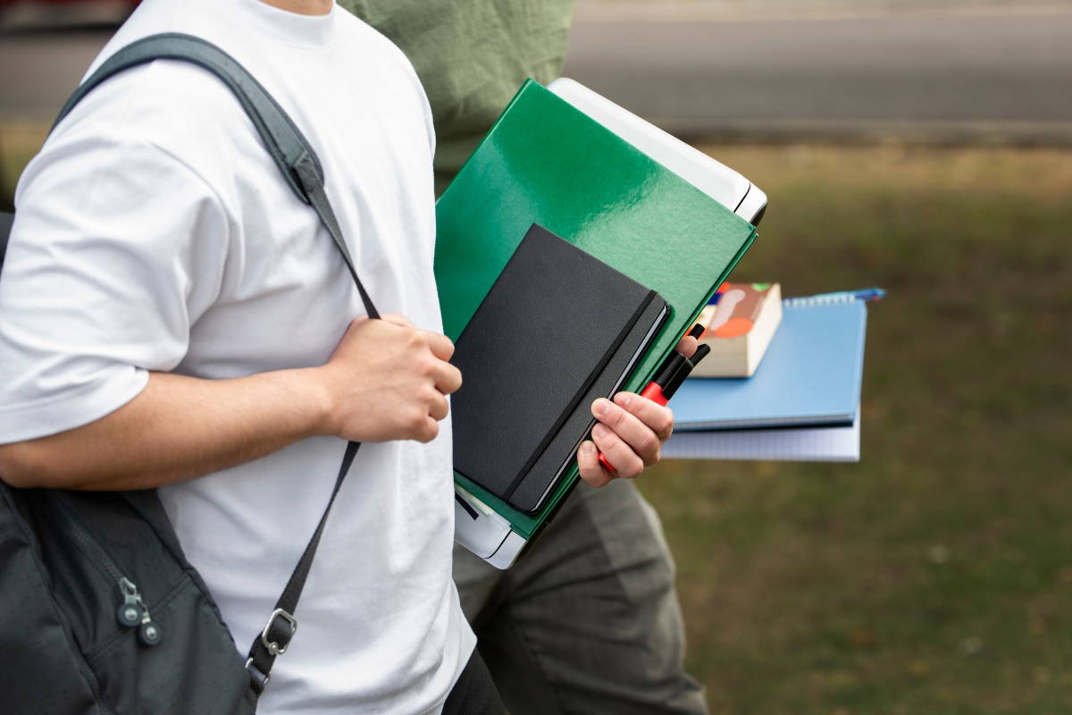 A student walking with notebooks and papers in hand.